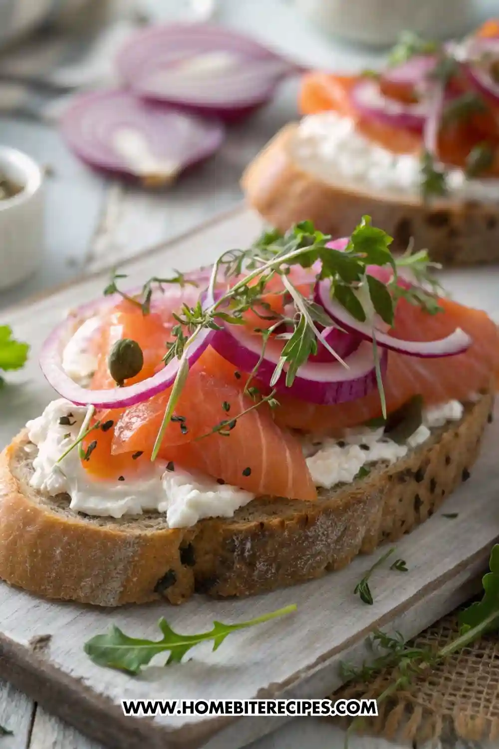 Smoked salmon toast topped with cream cheese, red onion slices, capers, fresh herbs, and black sesame seeds on rustic bread.