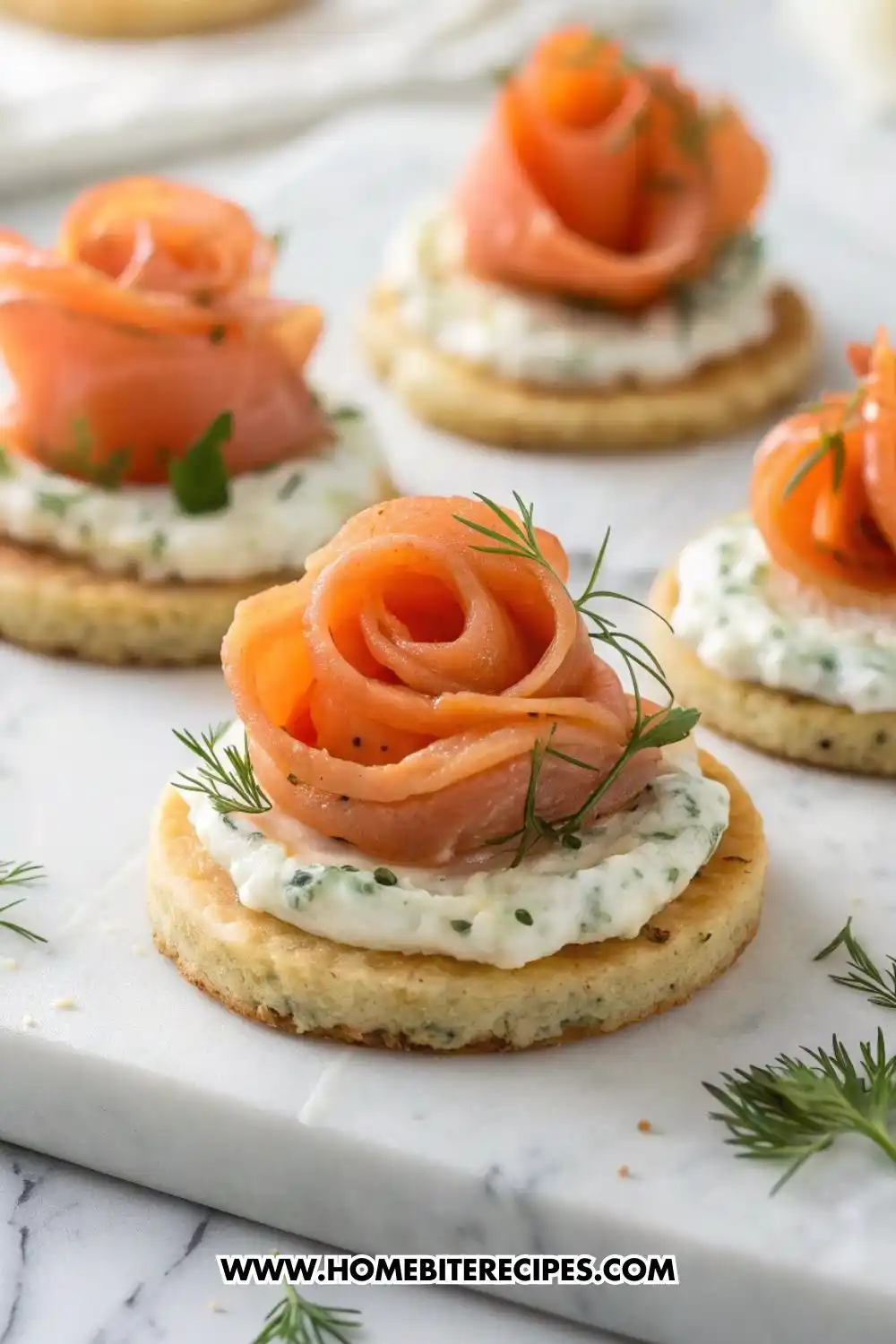 Close-up view of elegant smoked salmon rose canapés arranged on a marble surface, featuring thin slices of smoked salmon shaped into roses on top of herb cream cheese and round crackers, garnished with fresh dill.