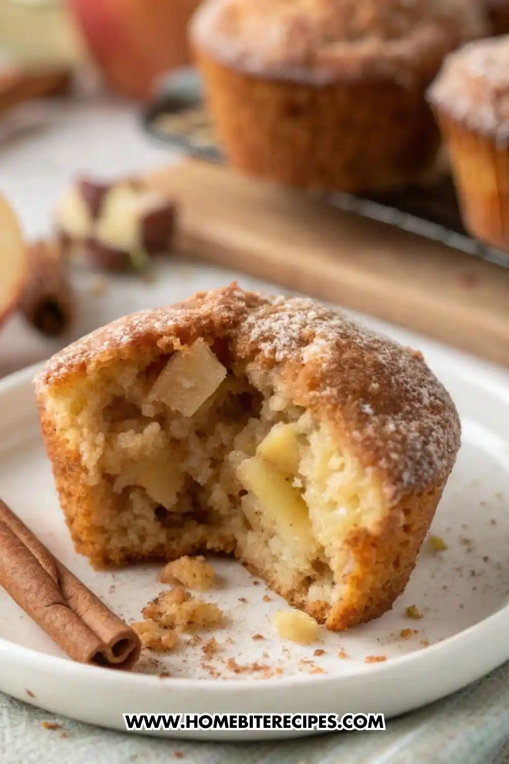 Moist apple cinnamon muffin broken open showing soft crumb and apple chunks, dusted with cinnamon sugar on a plate.