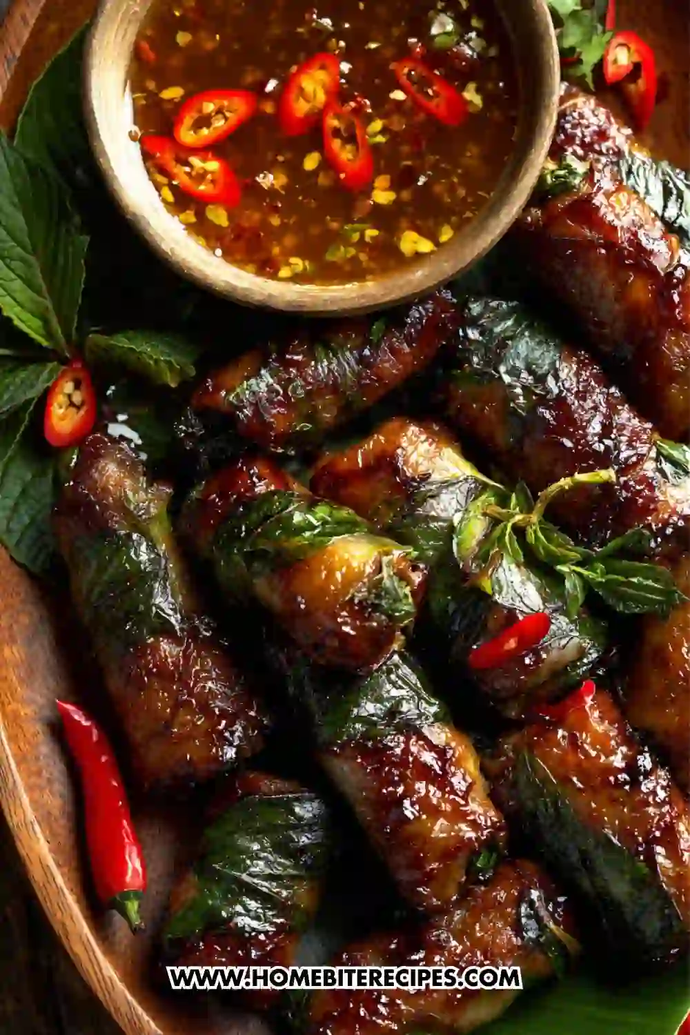 Close-up of Vietnamese basil beef rolls filled with crisp cabbage and beef, with a bowl of spicy chili dipping sauce on a wooden platter.