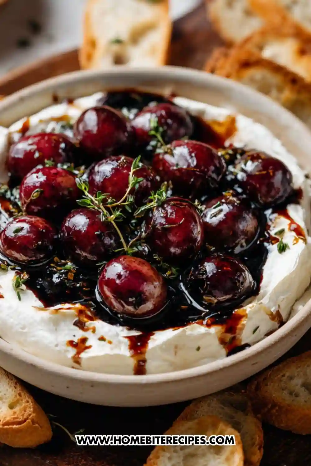 Creamy whipped brie dip in a ceramic bowl topped with glossy roasted balsamic grapes, drizzled with balsamic reduction and fresh thyme, surrounded by toasted baguette slices and rustic crackers