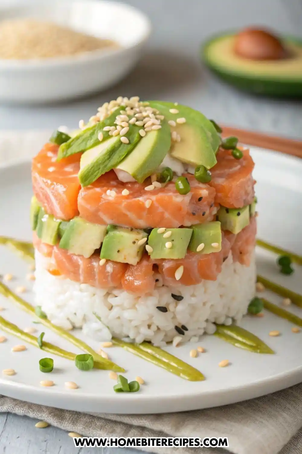 A gourmet stacked sushi tower on a white plate with layers of white sushi rice, diced fresh salmon, and cubed avocado, topped with avocado slices and sesame seeds.