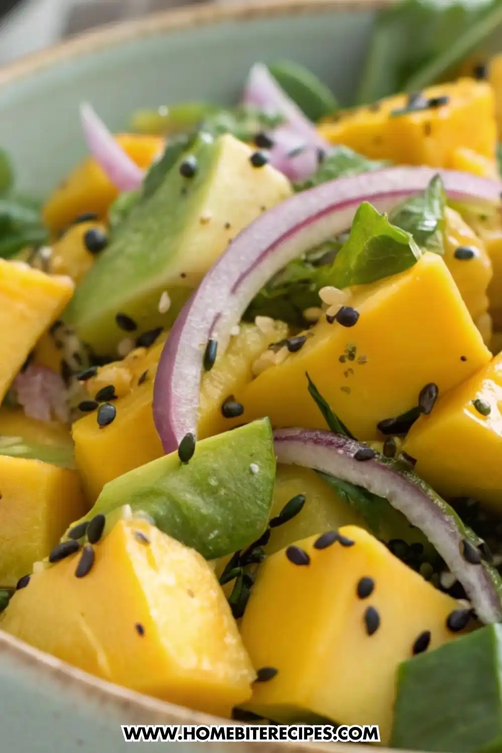 Fresh mango avocado salad with ripe mango cubes, avocado chunks, mixed greens, red onion, sesame seeds, and chili flakes in a ceramic bowl.