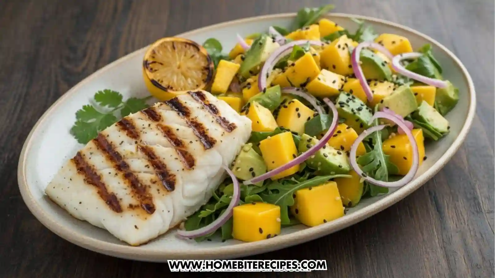A grilled white fish fillet with charred grill marks served on a plate next to a vibrant mango and avocado salad. The salad includes cubed mango, sliced avocado, red onion rings, and black sesame seeds on a bed of greens, garnished with a grilled lemon half.