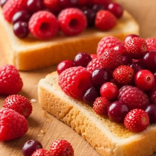 Close-up of two slices of toasted bread topped with fresh mixed berries including raspberries, strawberries, and cranberries on a wooden board.