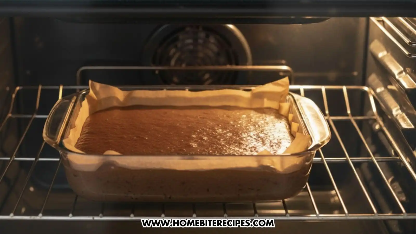 A glass rectangular baking dish containing brownie batter sits on the center rack of a preheated oven. The dish is lined with parchment paper, and the brownies are beginning to rise and set.