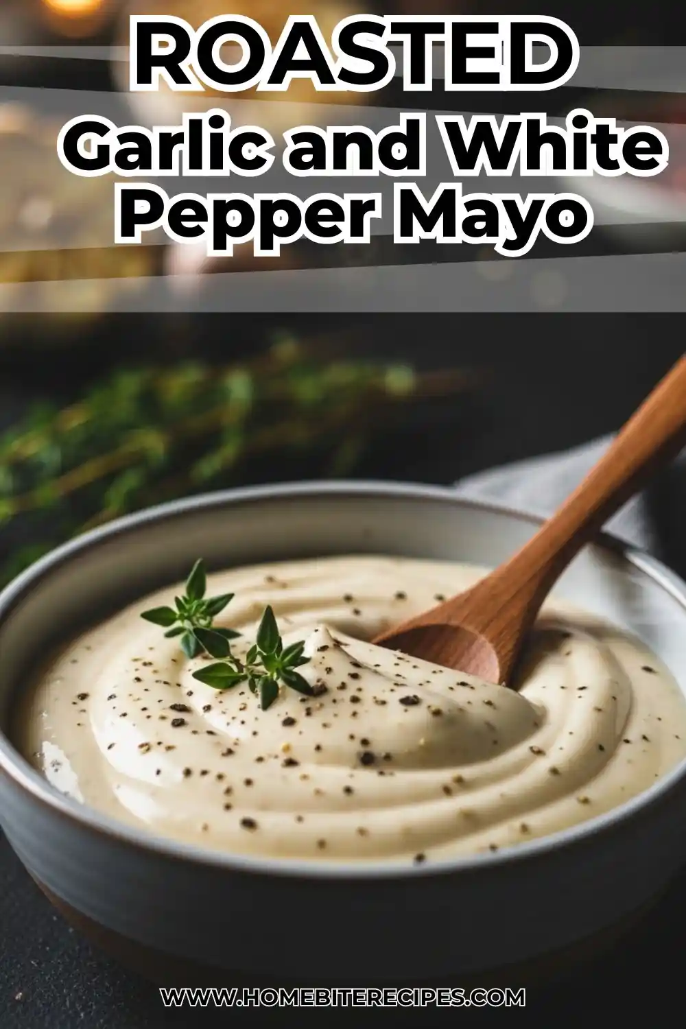 Creamy white roasted garlic mayo in a small bowl next to a caramelized head of roasted garlic on a dark stone surface.